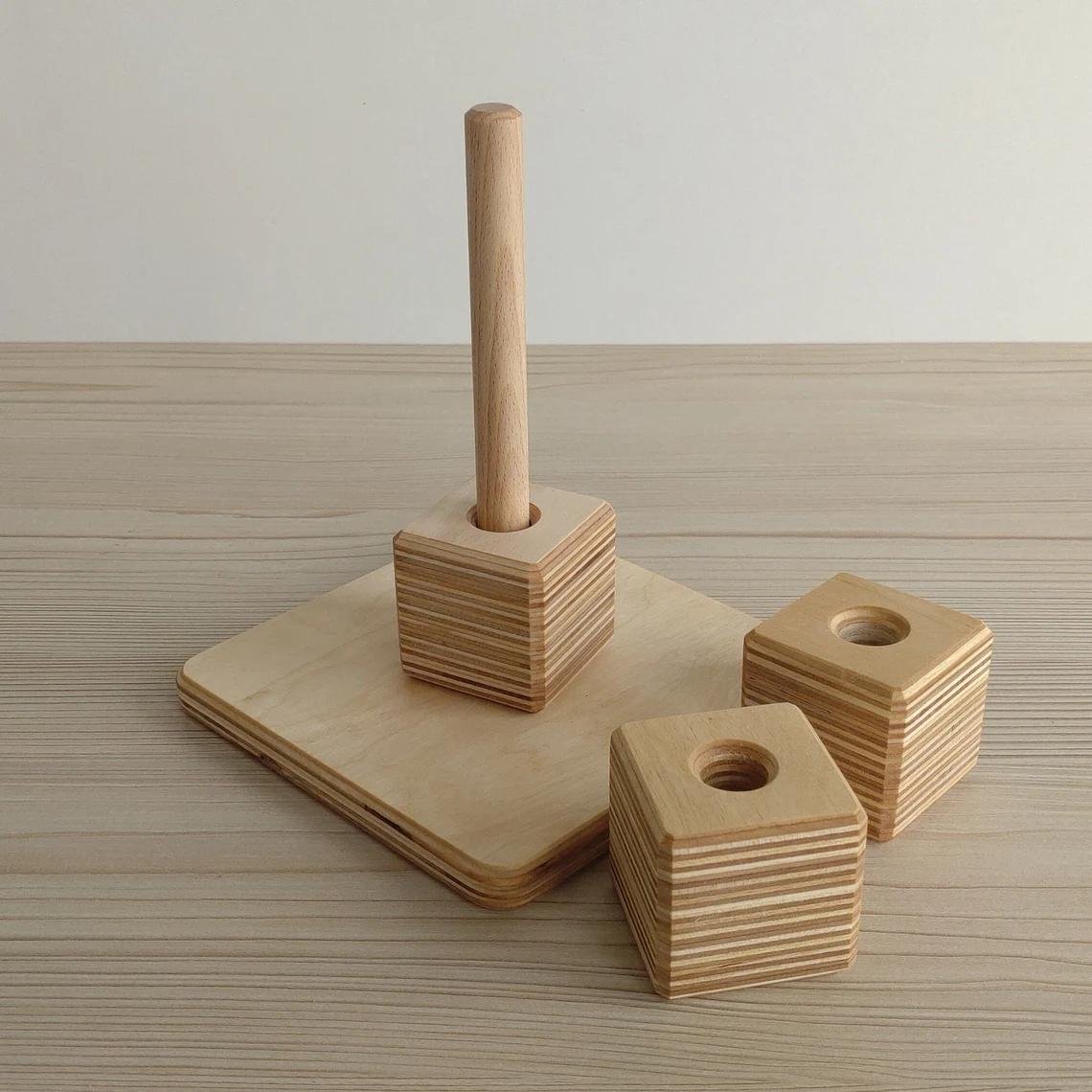 Montessori koka rotaļlieta ar trim kubiem uz vertikāla bērza stieņa un pamatnes.