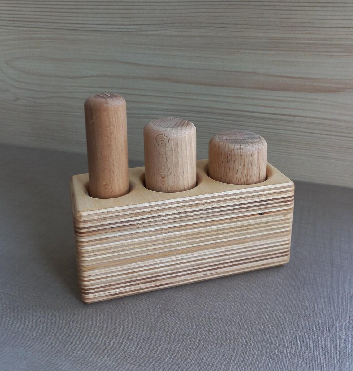 Montessori plaukstas satvēriena bloks ar trim dažāda izmēra dižskābarža cilindriem bērza pamatnē.