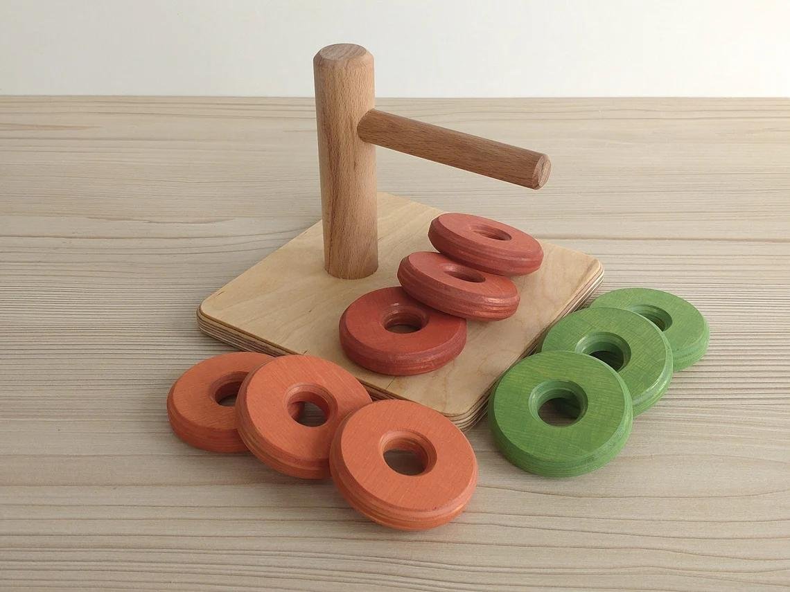 Montessori koka rotaļlieta ar trim krāsainiem diskiem uz horizontāla bērza stieņa.